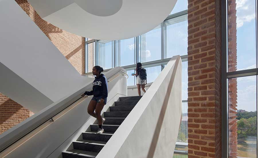 At the building’s main entrance, a cantilevered sculptural stair is framed by brick and a fritted glass wall.